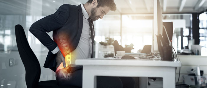 man holding lower back in pain while sitting at his desk