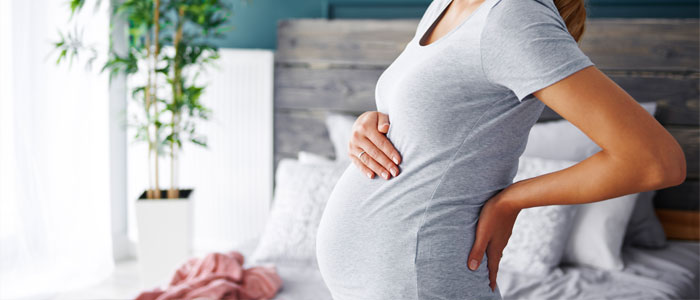 A pregnant woman supporting her back with one hand and resting her other hand on her stomach